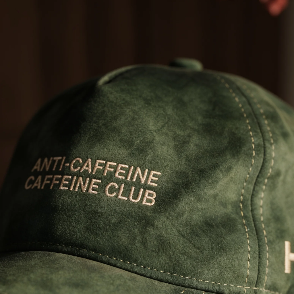 Green cap with 'ANTI-CAFFEINE CAFFEINE CLUB' text on a dark background