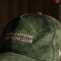 Green cap with 'ANTI-CAFFEINE CAFFEINE CLUB' text on a dark background