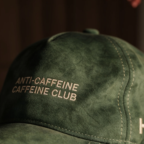Green cap with 'ANTI-CAFFEINE CAFFEINE CLUB' text on a dark background