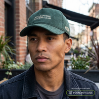 Man wearing a green cap with text, standing outdoors.
